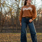 Woman standing in woods wearing a sweater and jeans 