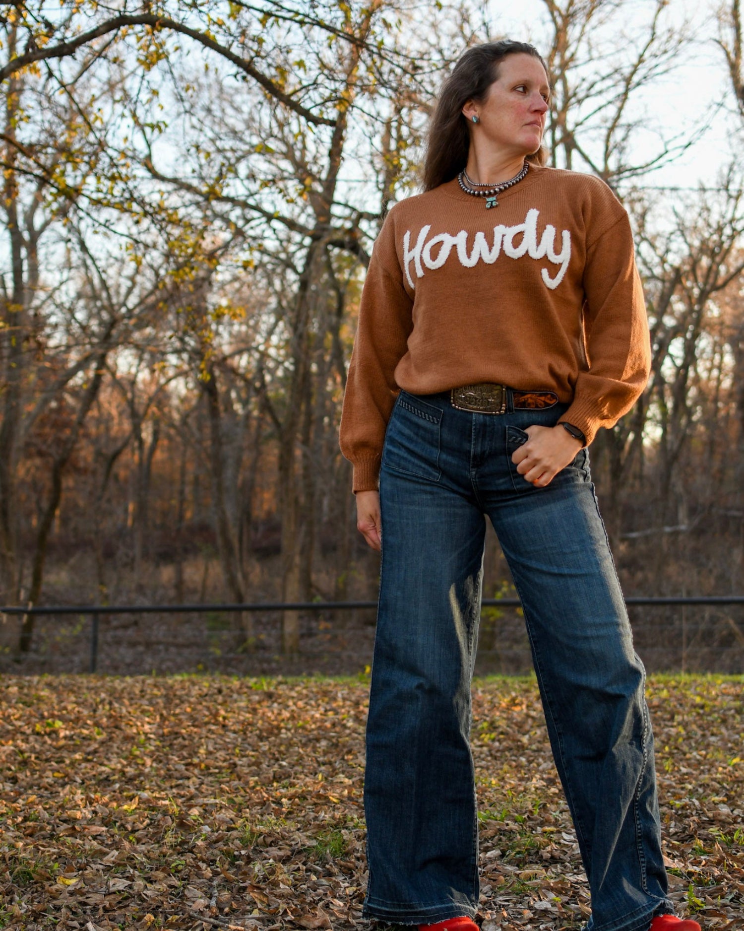 Woman standing in woods wearing a sweater and jeans 