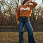Model wearing howdy sweater and jeans standing in leaves