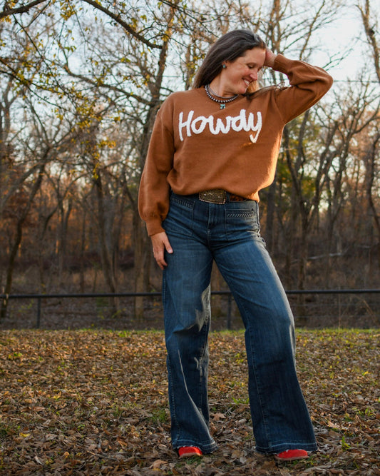 Model wearing howdy sweater and jeans standing in leaves