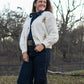 woman standing in front of trees wearing jeans and a cardigan sweater