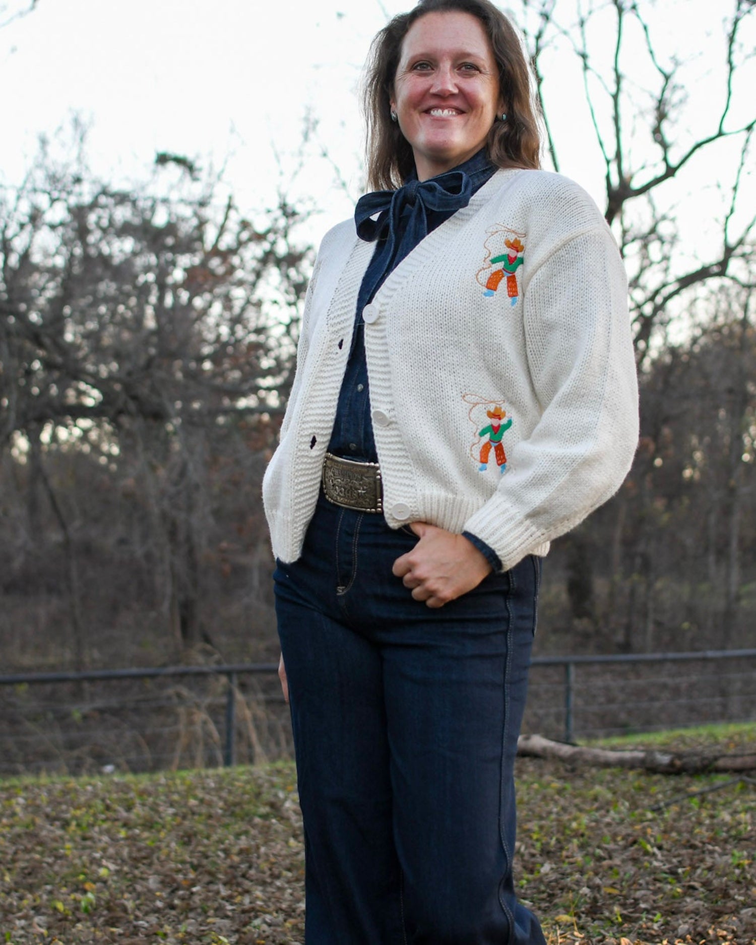 woman in trees wearing a cardigan sweater and jeans 
