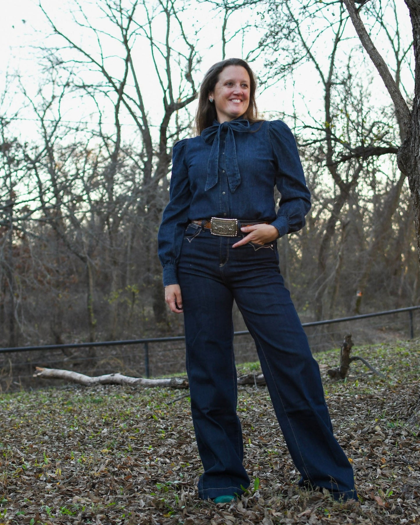 Woman wearing a blouse and jeans with trees in the background