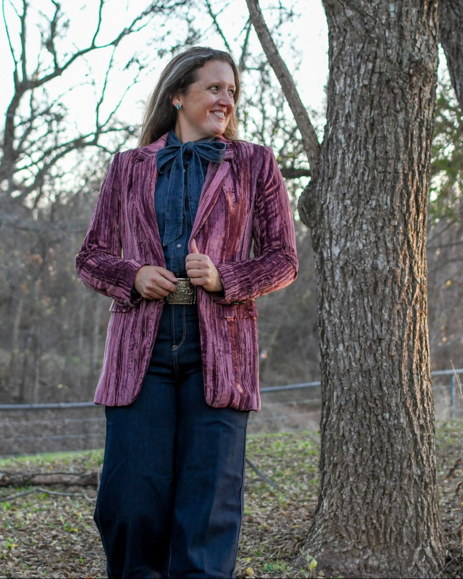 Model standing in trees wearing a blazer and jeans