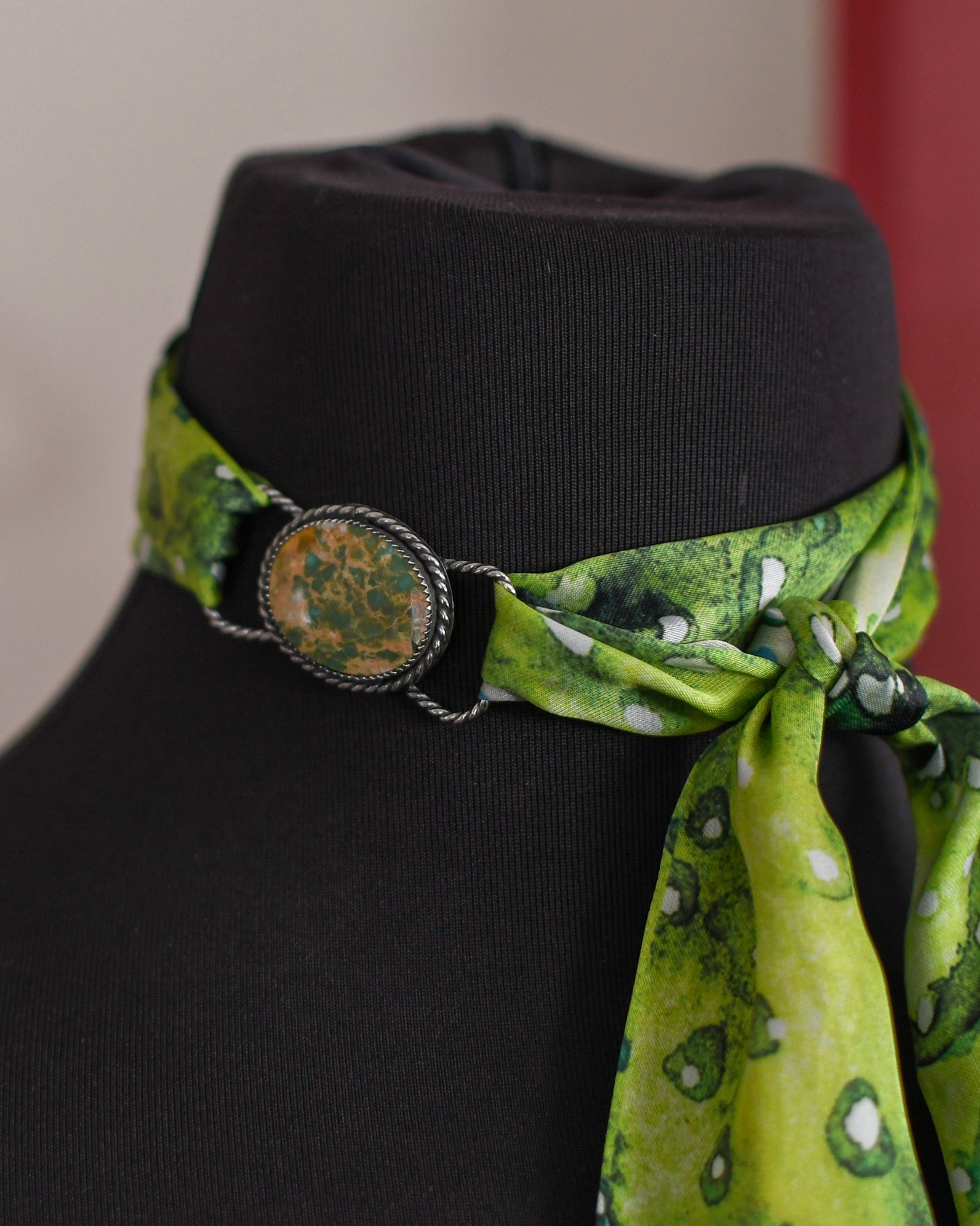 Green patterned scarf tied around a black mannequin head with a blurred background