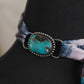 Black mannequin with a decorative scarf featuring a turquoise stone and patterned fabric.