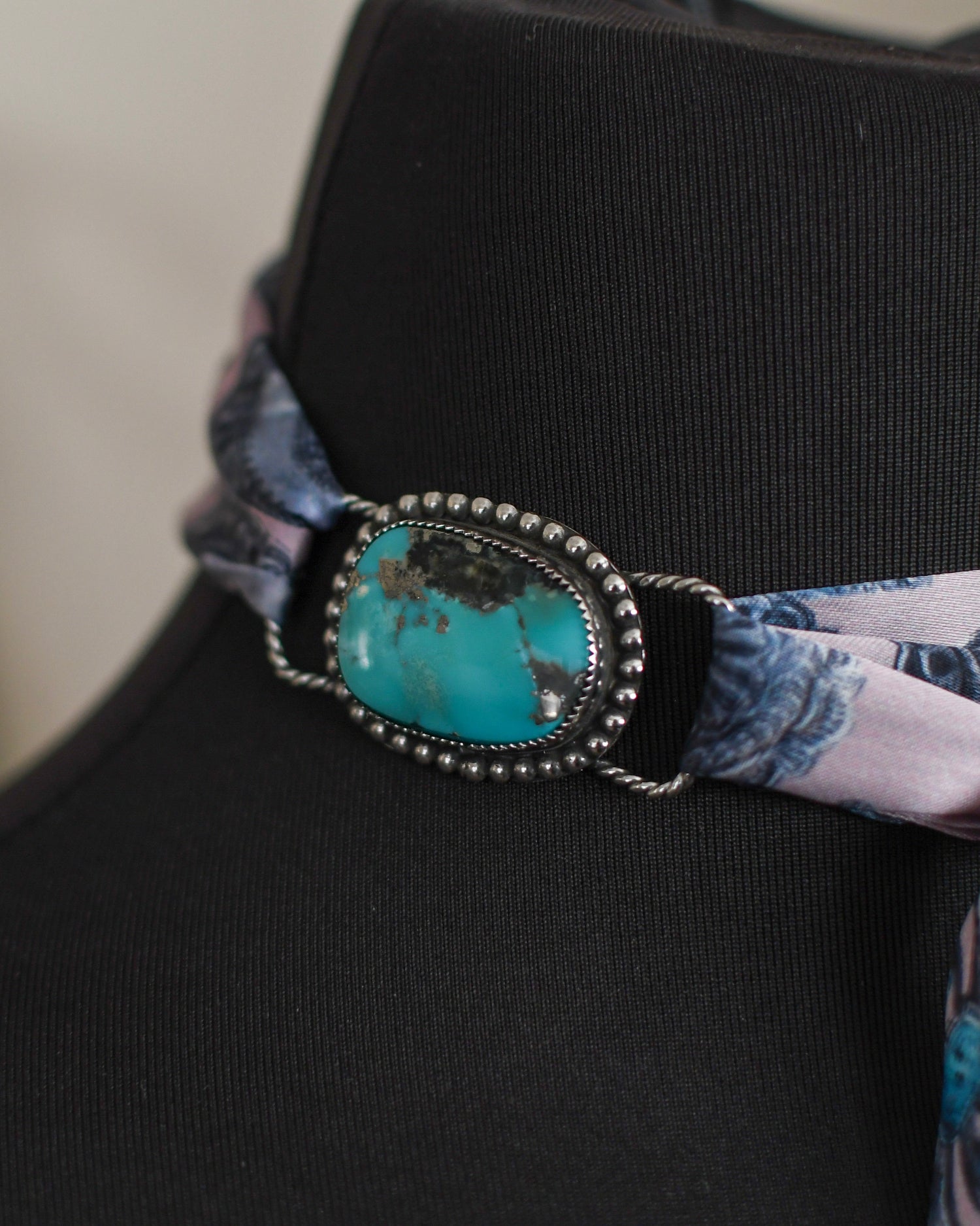 Black mannequin with a decorative scarf featuring a turquoise stone and patterned fabric.
