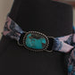 Black mannequin with a decorative band featuring a turquoise stone and pink fabric 