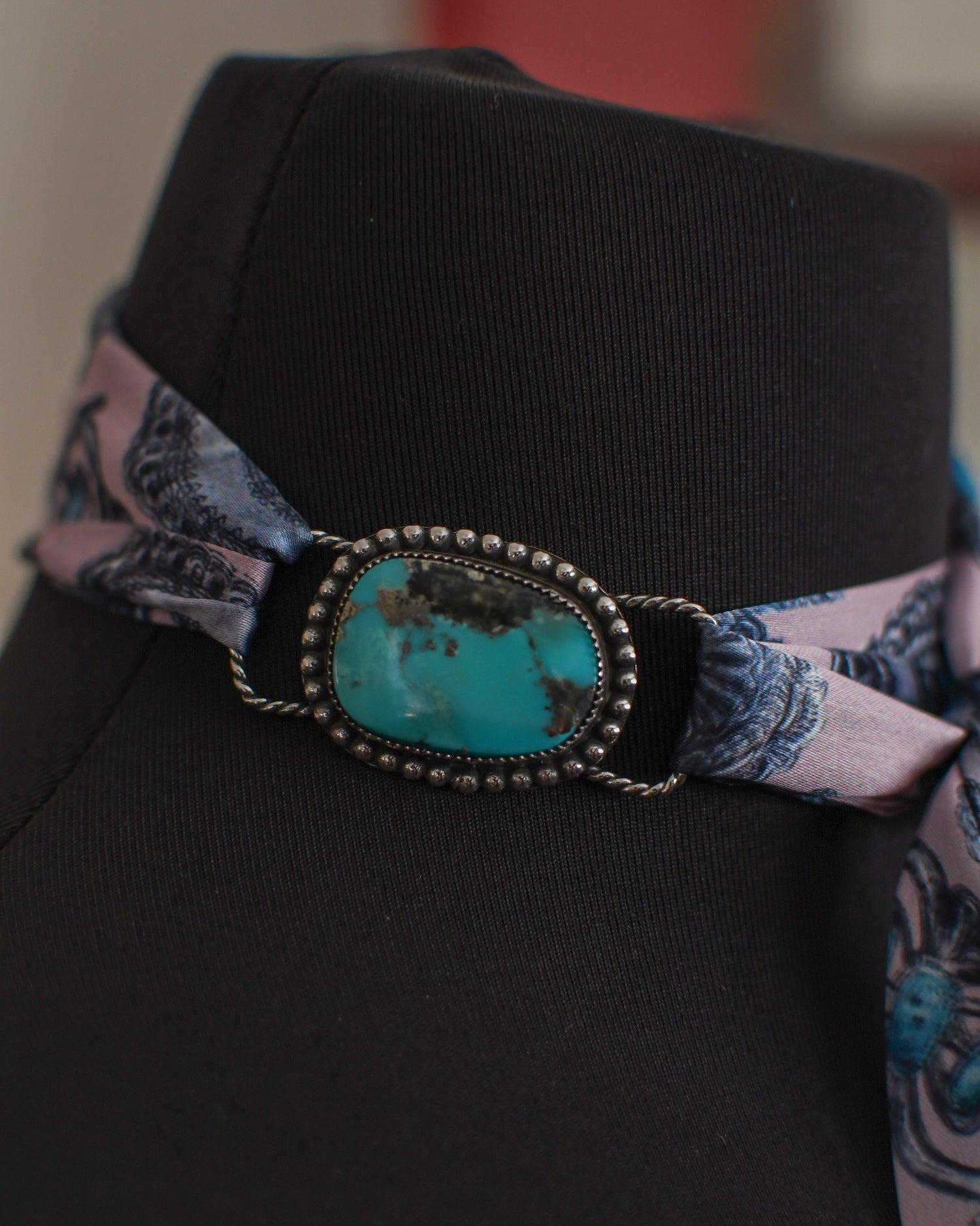 Black mannequin with a decorative band featuring a turquoise stone and pink fabric 