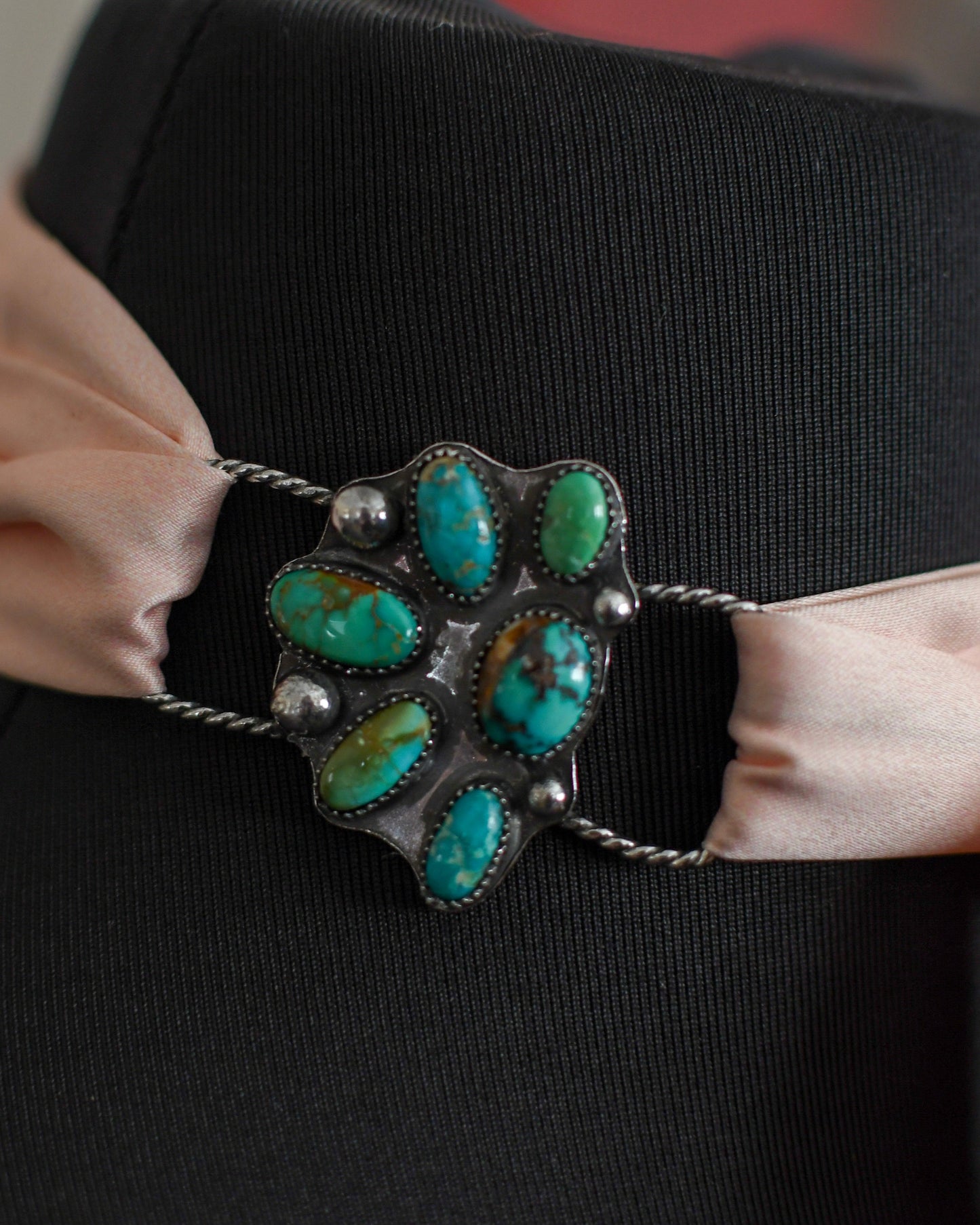 mannequin with a decorative brooch featuring turquoise stones and a pink ribbon.
