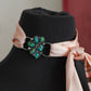 mannequin with a decorative band featuring turquoise stones and a pink scarf on a blurred background