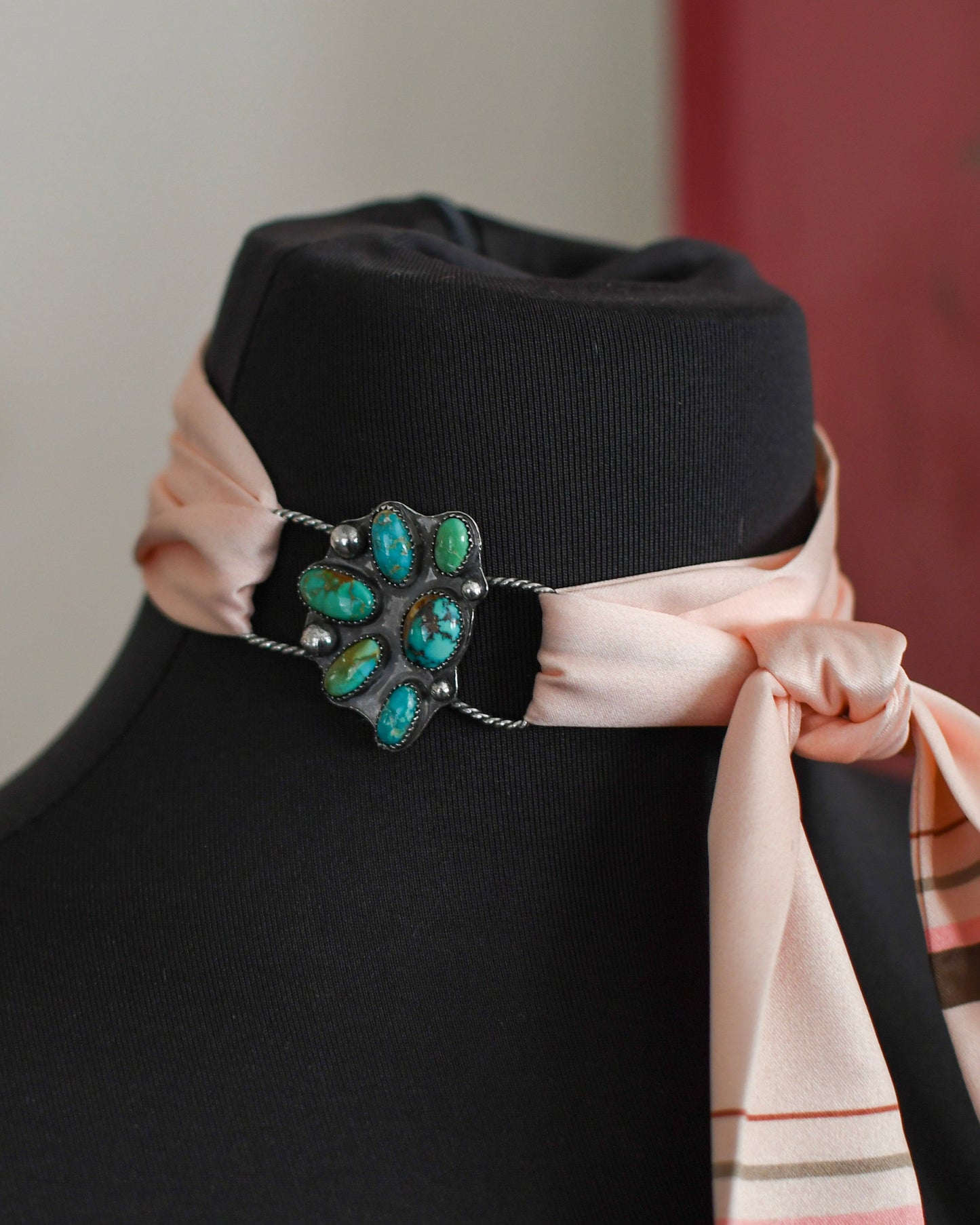 mannequin with a decorative band featuring turquoise stones and a pink scarf on a blurred background