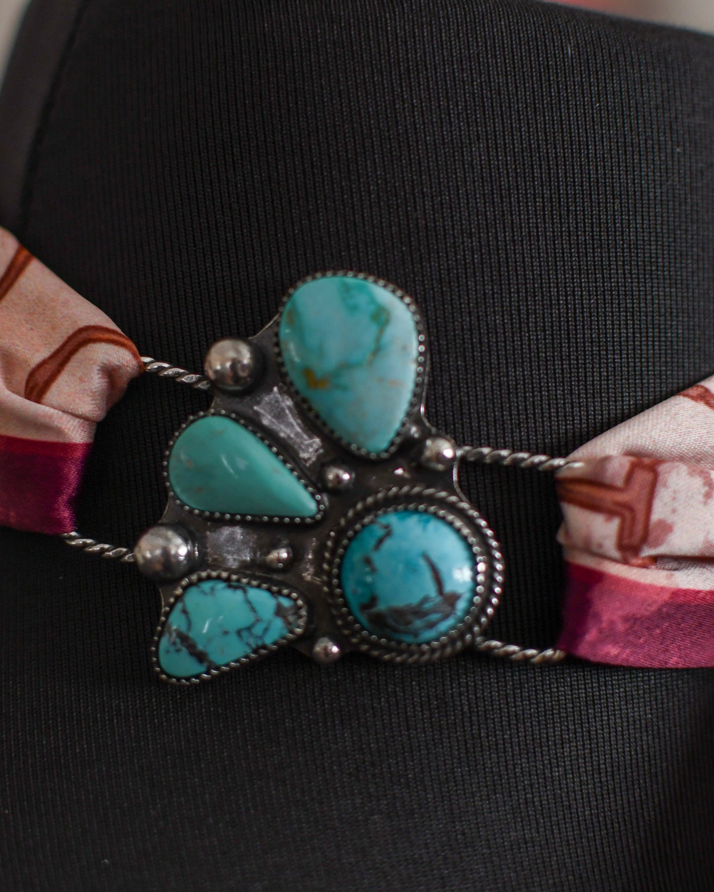 Turquoise stone twilly slide on a black mannequin with a patterned fabric strap.