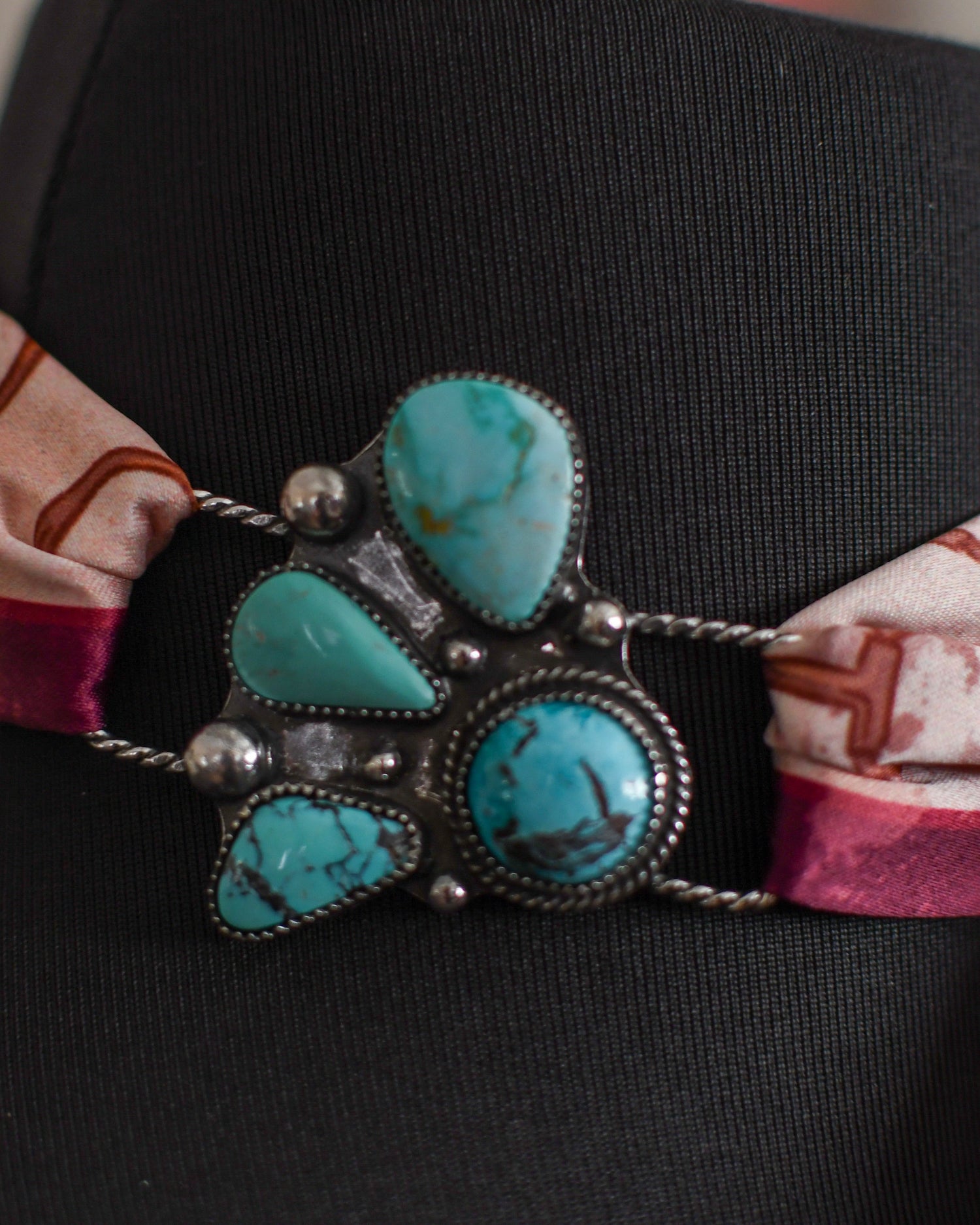 Turquoise stone twilly slide on a black mannequin with a patterned fabric strap.
