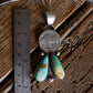 Silver pendant with turquoise stones next to a ruler on a wooden surface