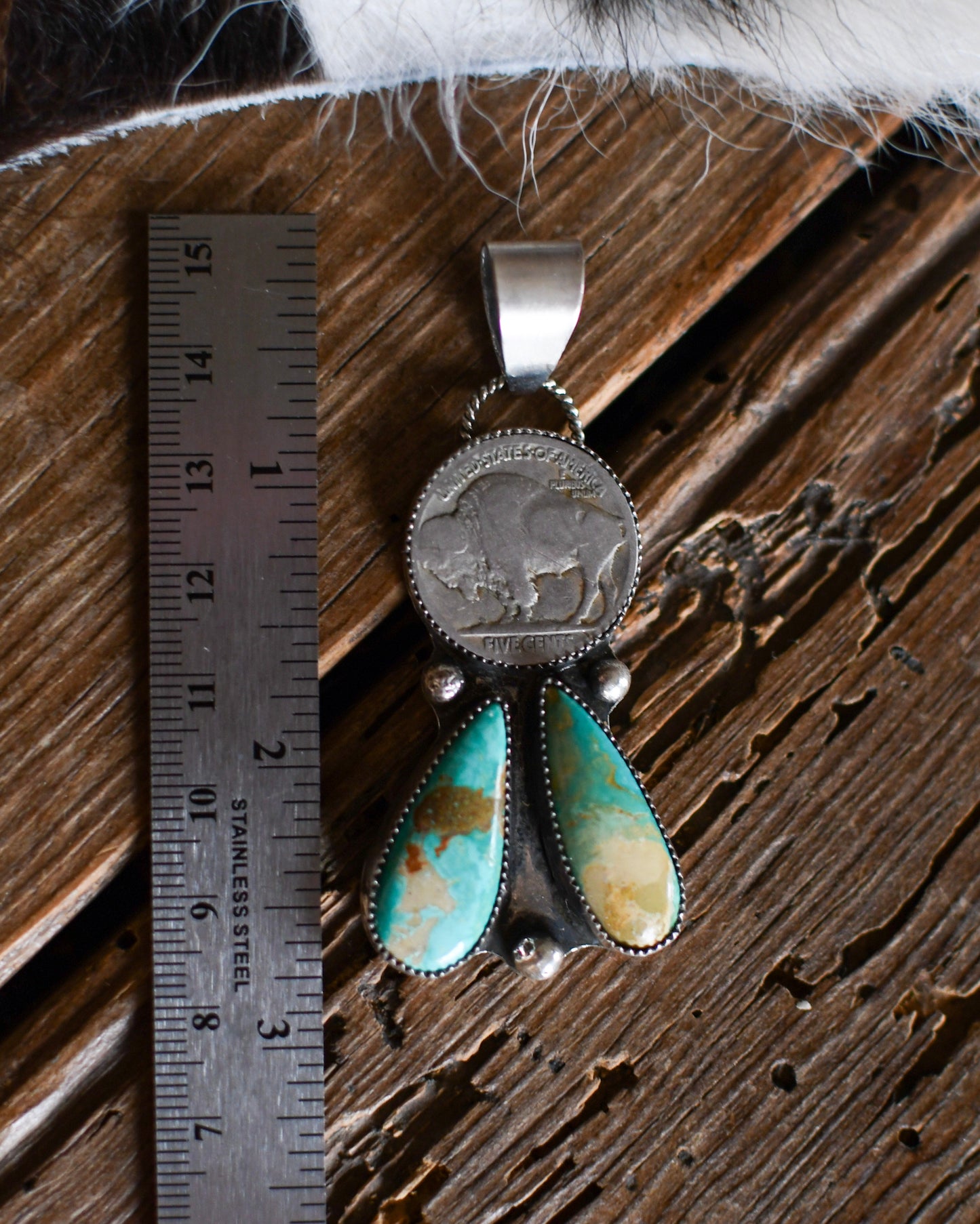 Silver pendant with turquoise stones next to a ruler on a wooden surface