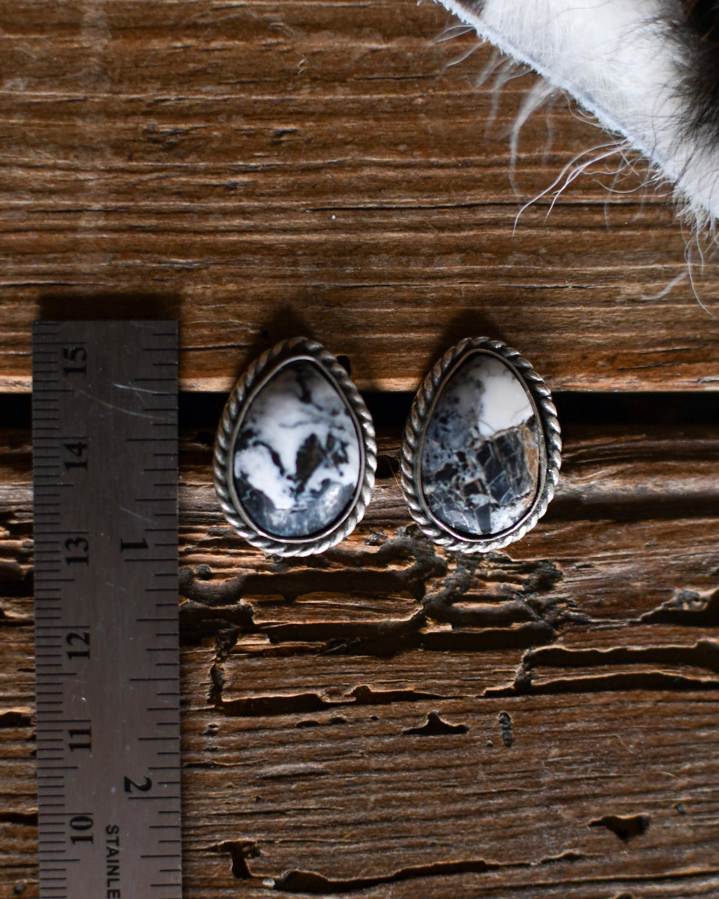 Pair of silver earrings with black and white stones on a wooden surface with a ruler for scale.