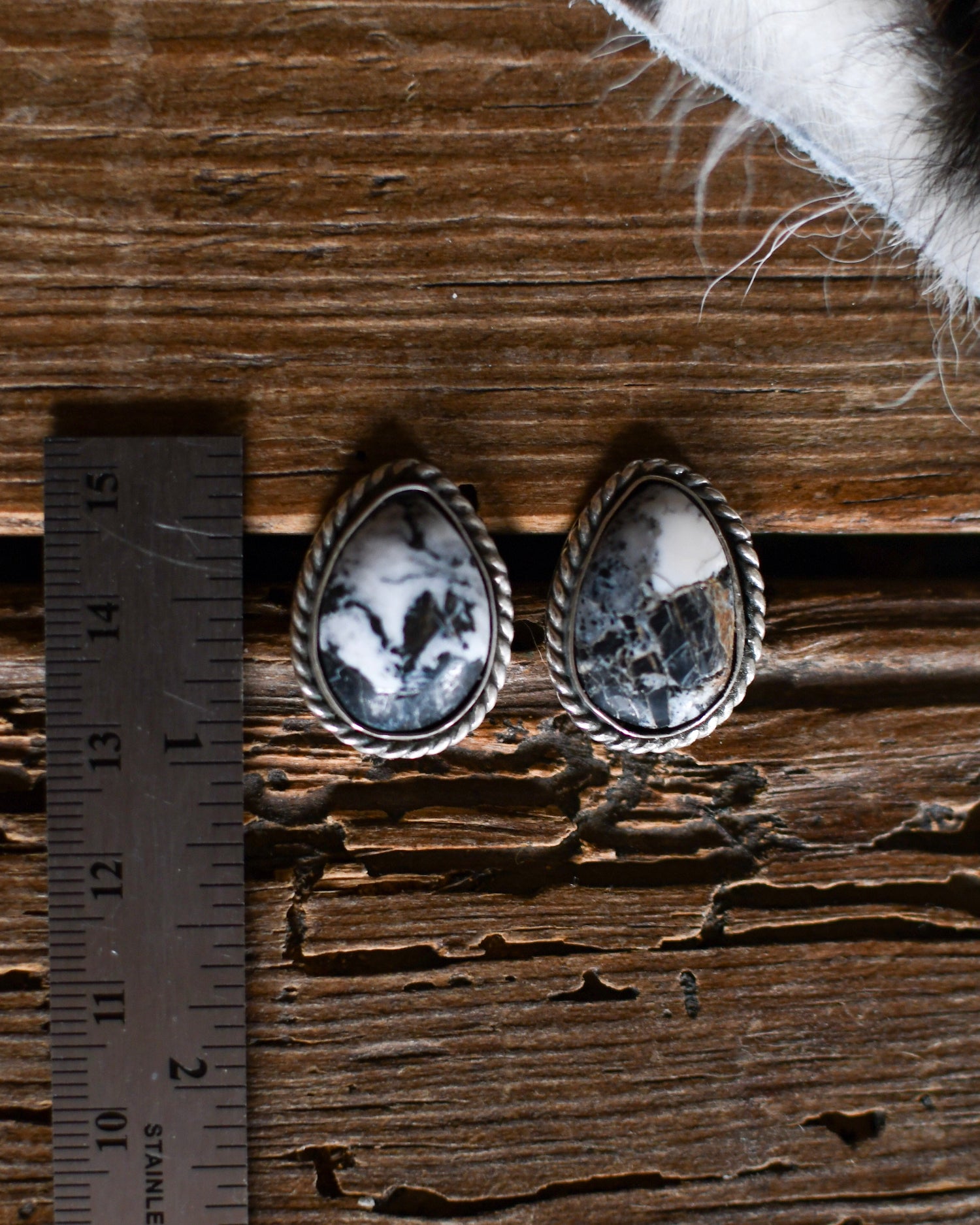 Pair of silver earrings with black and white stones on a wooden surface with a ruler for scale.