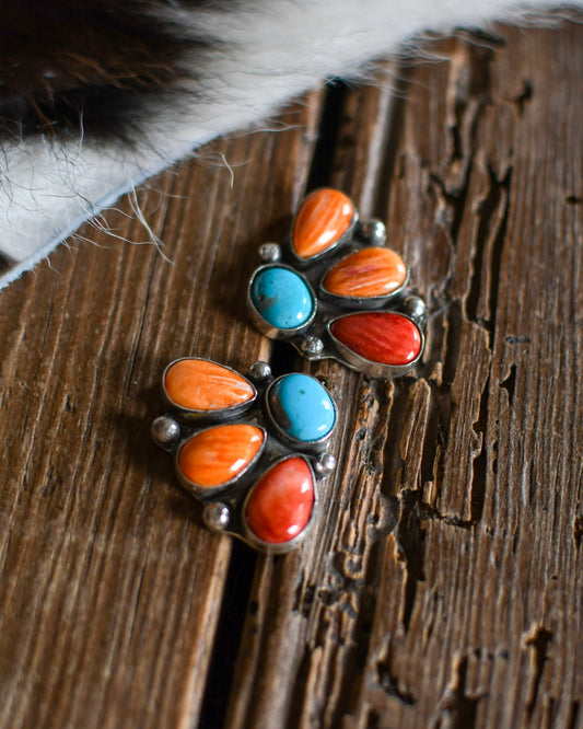 Pair of silver earrings with turquoise and orange stones on a wooden surface