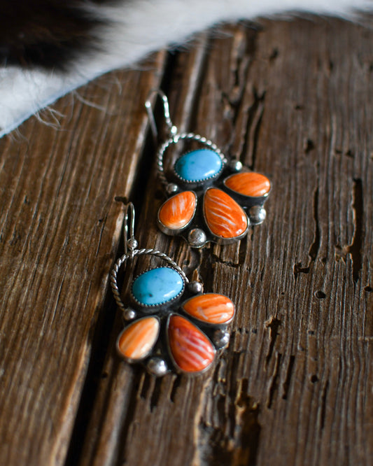 Pair of earrings with turquoise and orange stones on a wooden surface