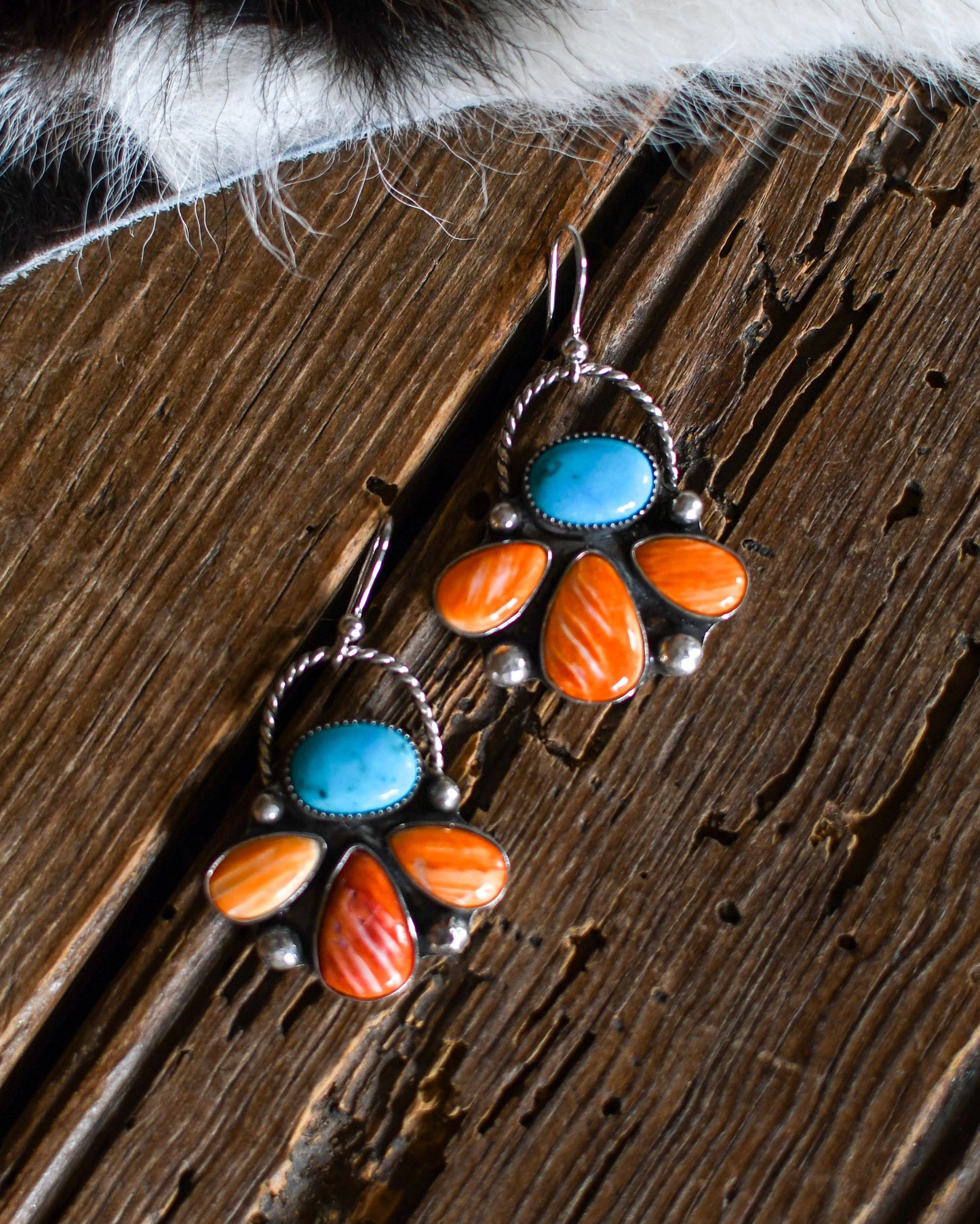 Pair of earrings with turquoise and orange stones on a wooden surface