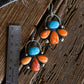 Pair of earrings with turquoise and orange stones on a wooden surface with a ruler for scale.