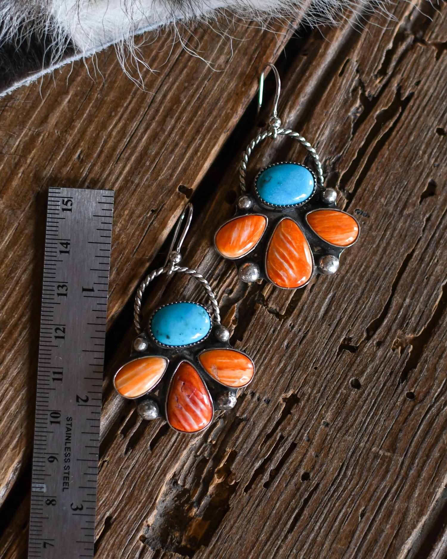 Pair of earrings with turquoise and orange stones on a wooden surface with a ruler for scale.
