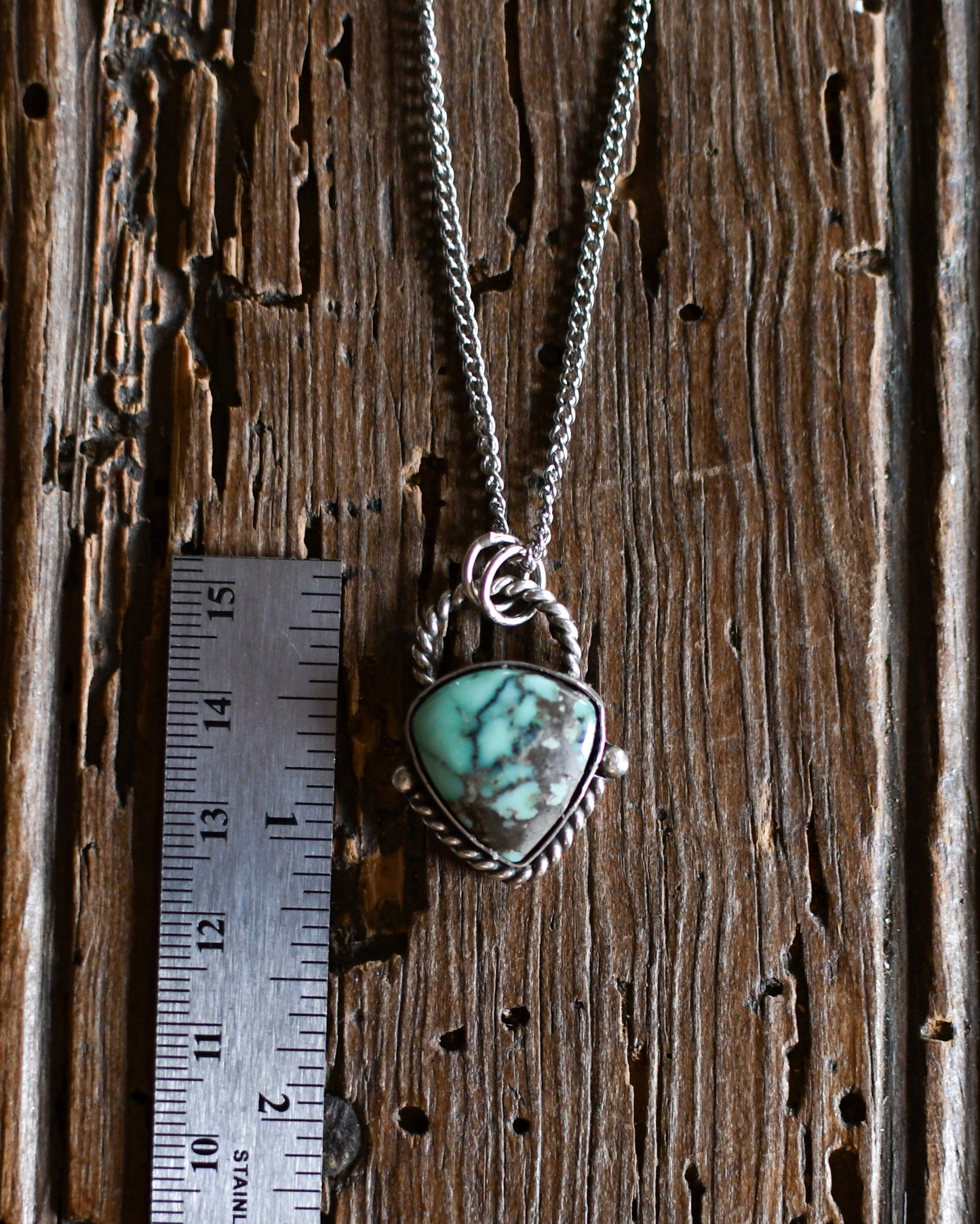 Necklace with a turquoise pendant on a wooden surface next to a ruler for scale.