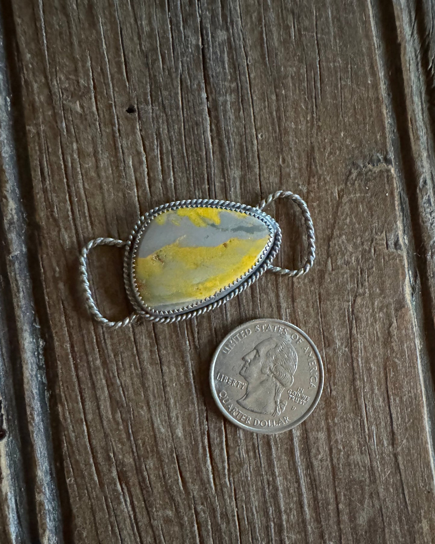 Silver twilly slide with yellow stone next to a quarter on wooden surface