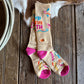 Colorful socks with text and patterns on a wooden surface next to a cow's leg.