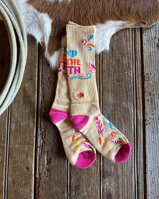 Colorful socks with text and patterns on a wooden surface next to a cow's leg.