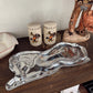 Decorative items including a silver tray, ceramic jars, and a wooden horse figure on a wooden surface.