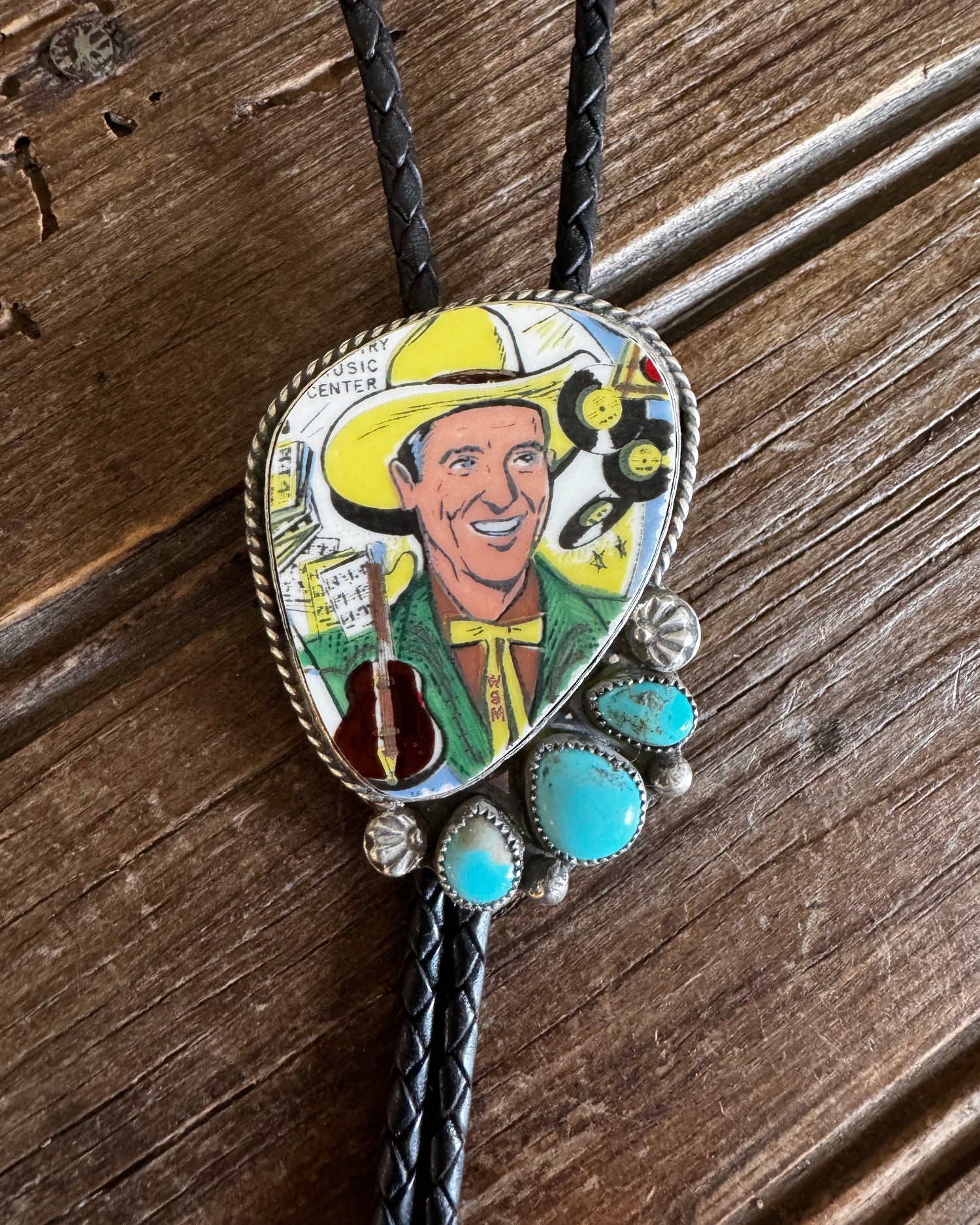 Bolo tie with a colorful design of a smiling man in a cowboy hat on a wooden surface