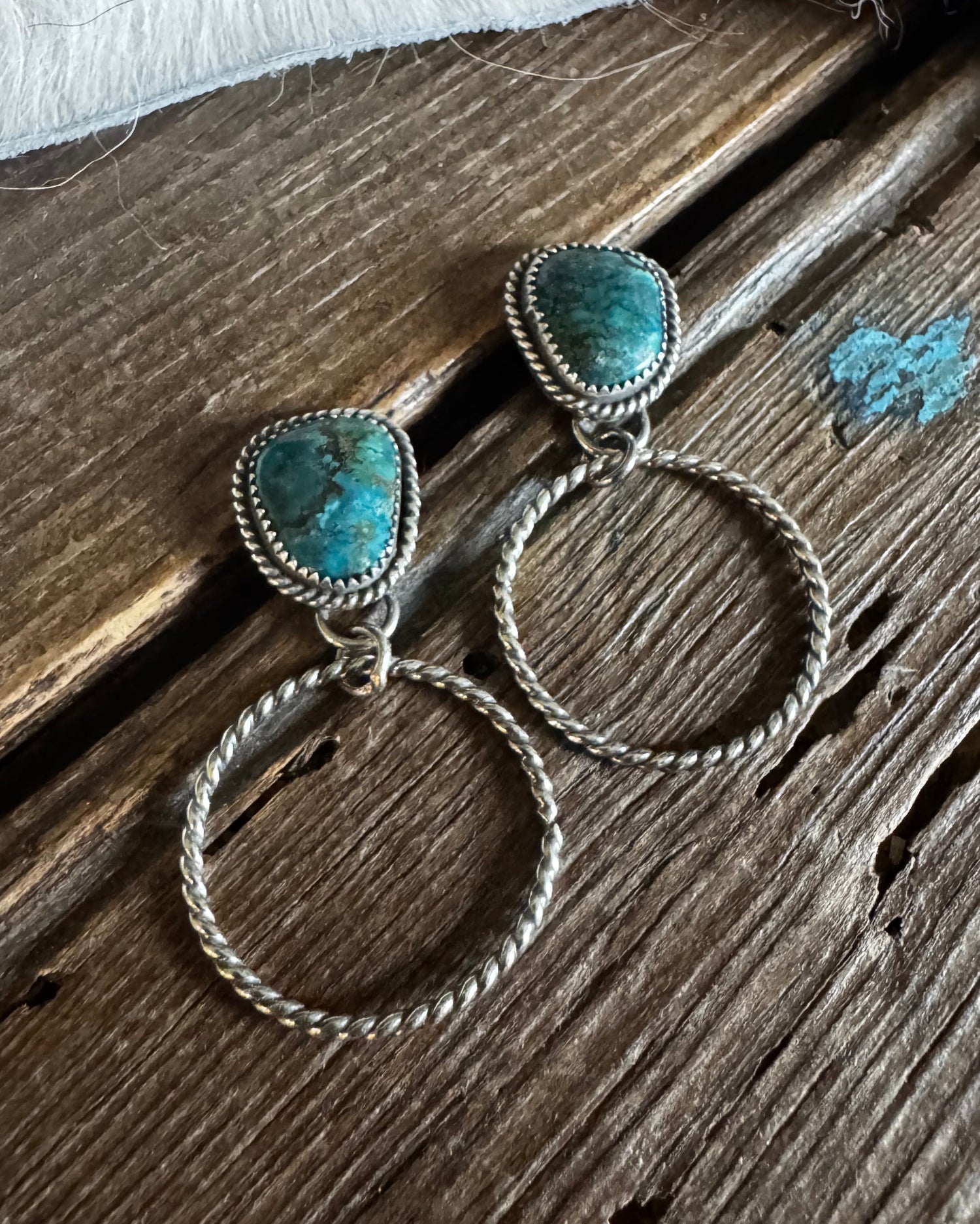 Silver hoop earrings with turquoise stones on a wooden surface