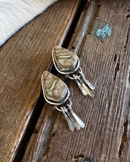 Pair of silver earrings with stone inlays on a wooden surface