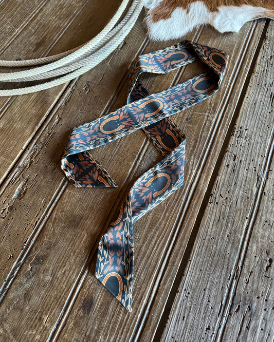 Ribbon scarf with horseshoes on a rustic wood background with a cowhide and rope
