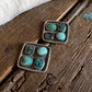 Pair of square earrings with turquoise stones on a wooden surface