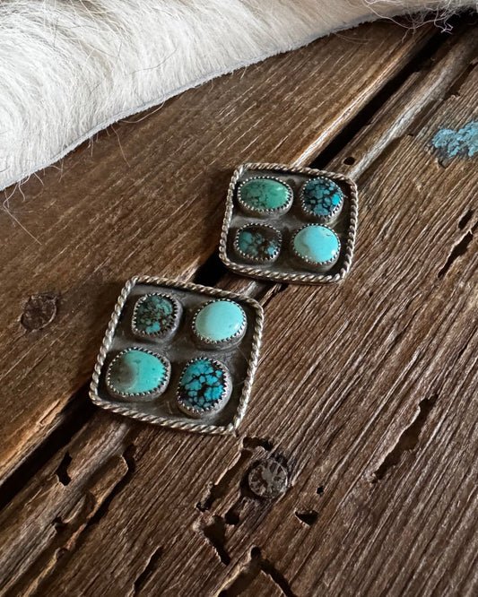 Pair of square earrings with turquoise stones on a wooden surface