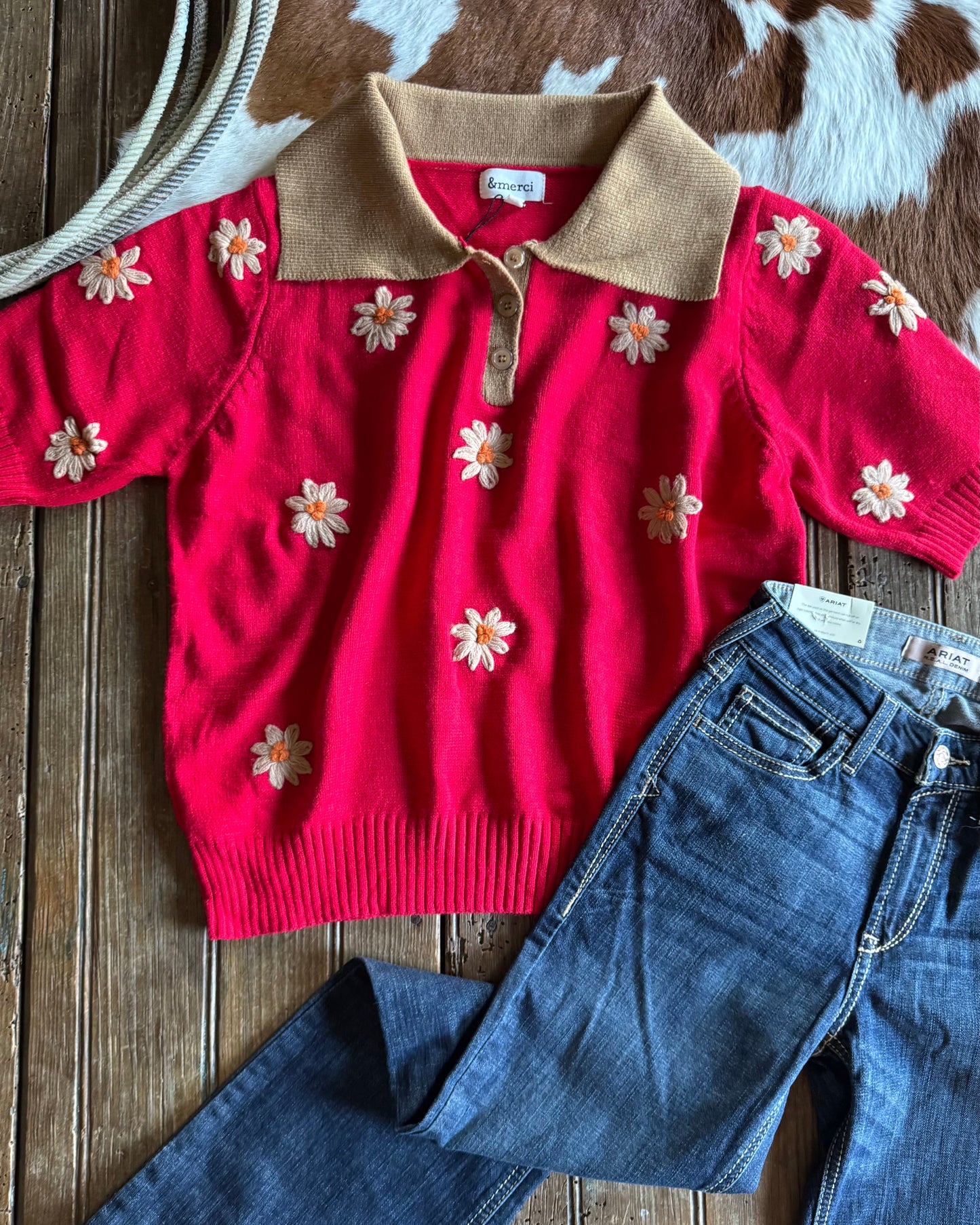 Red sweater with floral patterns and blue jeans on a wooden surface