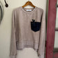 Folded beige sweater on a wooden hanger against a white wall.