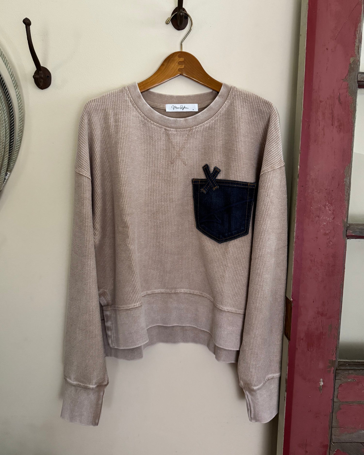 Folded beige sweater on a wooden hanger against a white wall.