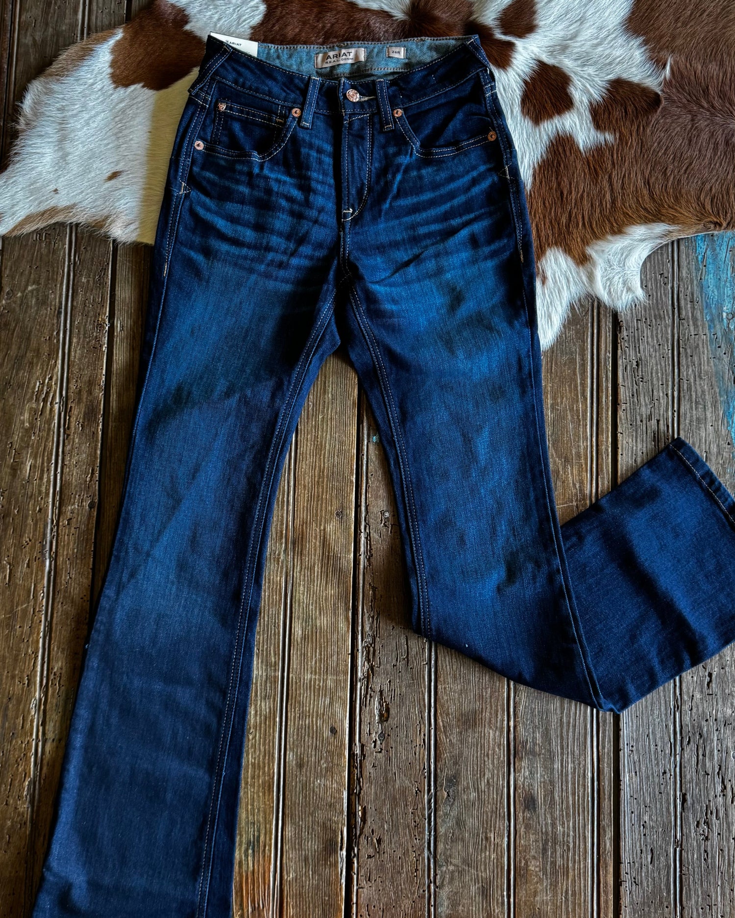 Blue jeans on a wooden table with a cowhide rug in the background