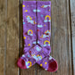 Lucky Unicorns Performance Socks in purple showing design on rustic wood background 