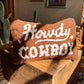 Pillow with 'Howdy, Cowboy' text on a wooden surface