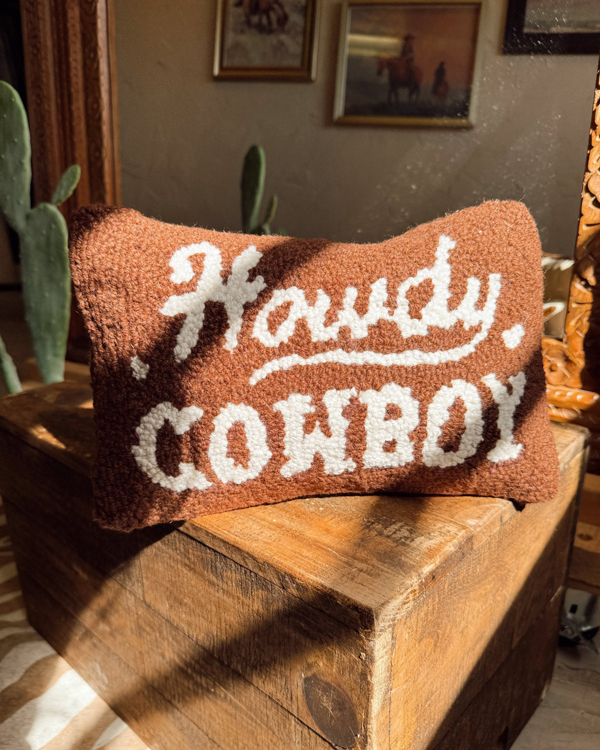 Pillow with 'Howdy, Cowboy' text on a wooden surface