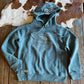 Blue hoodie with a graphic design on a wooden surface next to a cowhide rug