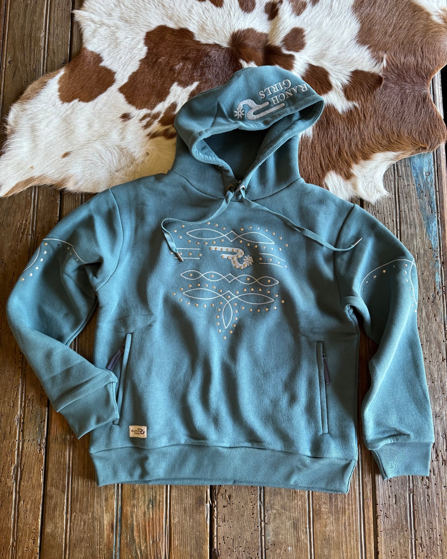 Blue hoodie with a graphic design on a wooden surface next to a cowhide rug