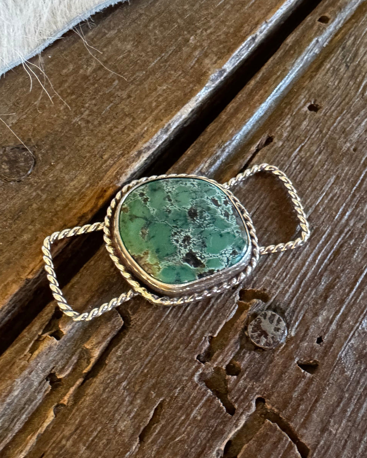 A silver-toned slide with a green stone, resting on a rustic dark wood surface with a white fur trim visible at the top.