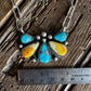 Necklace with turquoise and yellow stone pendant on a wooden surface with a ruler for scale.