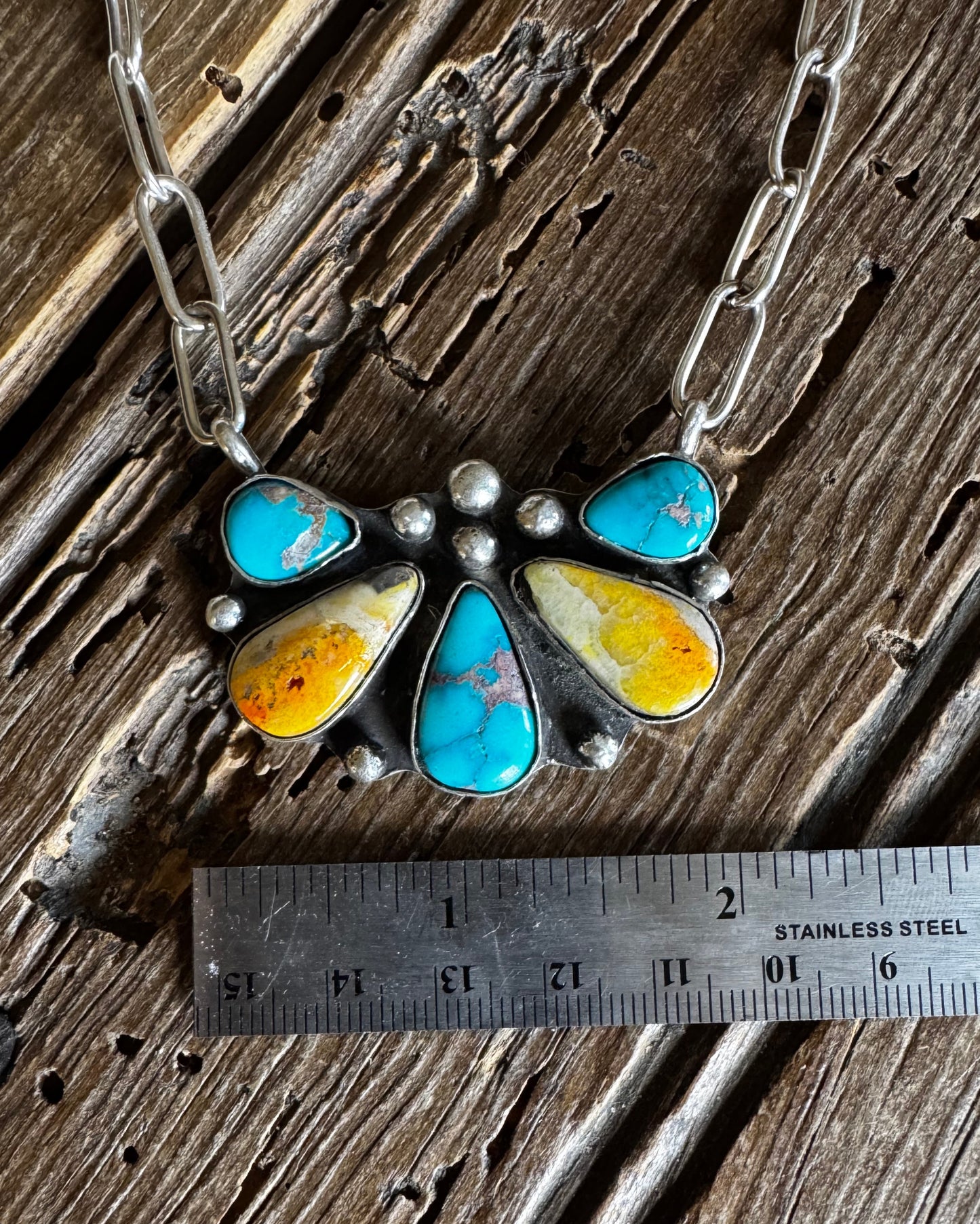 Necklace with turquoise and yellow stone pendant on a wooden surface with a ruler for scale.